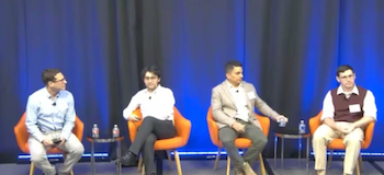 2025 Fintech Conference panel of academic speakers; 4 men sitting in chairs on a stage with blue curtains in background