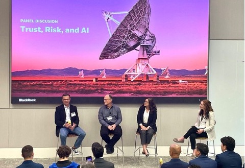 Panel speakers on a stage with large screen in background and audience facing them