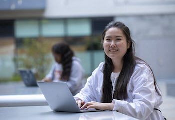 Female student smiling and with hands on laptop 