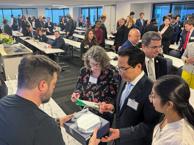 2025 International Business Ethics Case Competition at SFSU Downtown Campus, attendees walking around and seated at tables in a large meeting room with windows