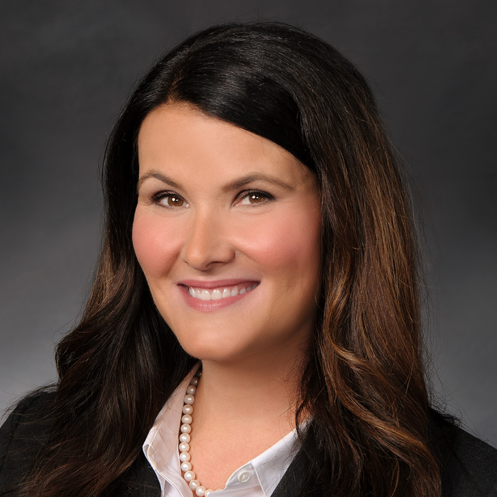 Erica Taylor, woman smiling with dark, long hair wearing white blouse and black suit jacket