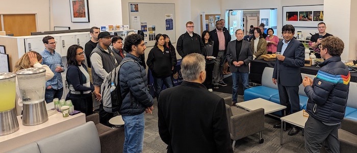 students and professors standing in a large room, food buffet table in background