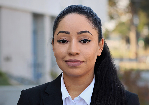 Student with dark hair up in a pony tail, wearing makeup, black suit jacket and white collared shirt