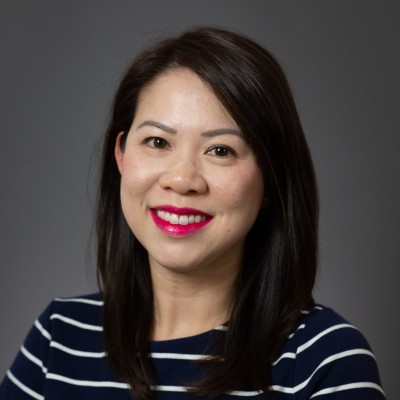 headshot of woman with red lipstick, dark medium-length hair, dark top with white stripes. gray background