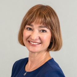 Headshot of smiling woman with short light brown wearing a blue top or dress