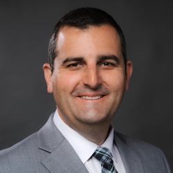 Headshot of smiling man with short, dark hair, wearing gray suit jacket, blue tie, and white collared shirt